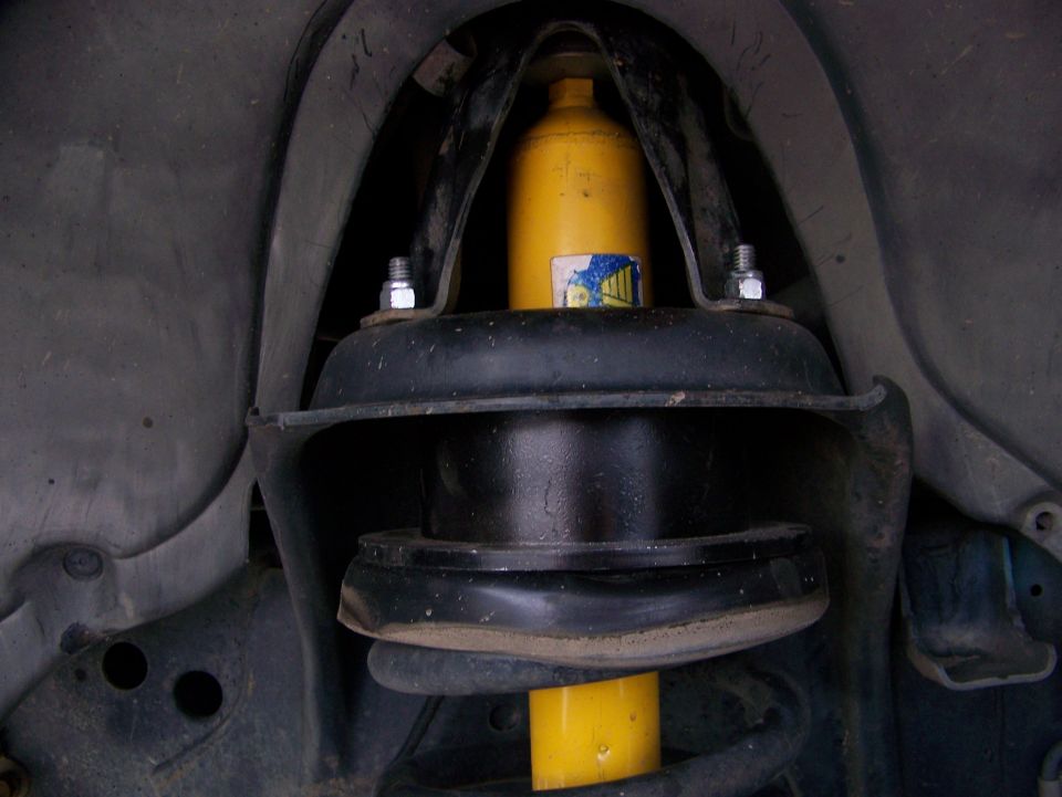 Yellow shock absorber and black coil spring installed in front suspension, viewed from underneath
