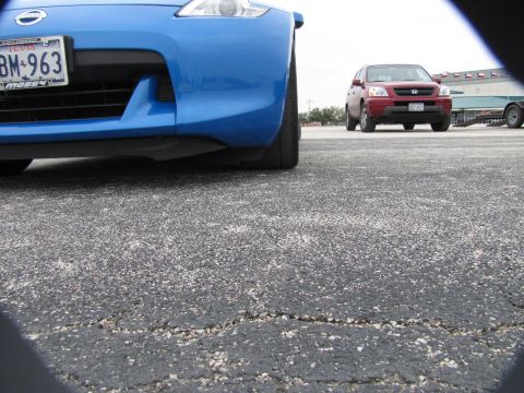 2003 Mazda Protege - Low angle shot of a blue car's front bumper with a red SUV in the distance.