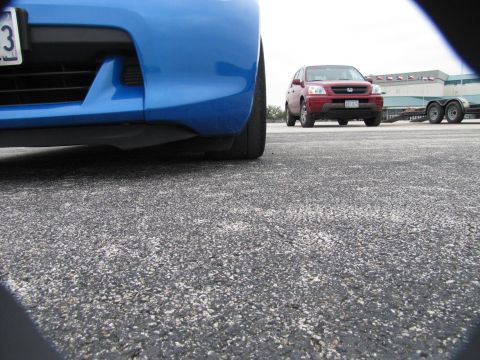 2003 Mazda Protege - A low angle shot of a blue car's front bumper with a red SUV and trailer in the distance.