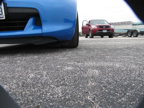 2003 Mazda Protege - A low-angle view of a blue car's front bumper and tire, with a red SUV and trailer visible in the distance.