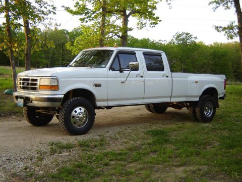 1994 Ford F-350 - This white Ford F-350 Super Duty dually pickup truck is seen from the side, parked on a dirt road with trees in the background.