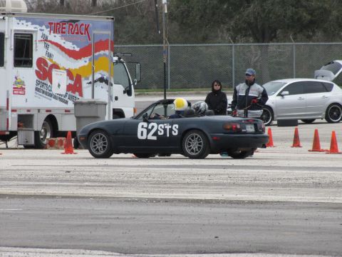 2003 Mazda Protege - A dark blue convertible with racing numbers is parked on a track, with a silver hatchback and a truck in the background.