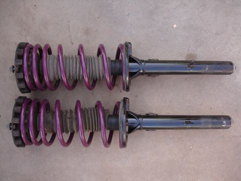 1995 Ford Taurus - A pair of aftermarket coilover suspension struts with purple springs are laid out on a concrete surface.