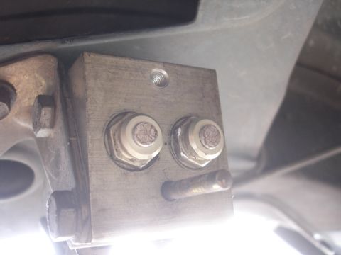 1995 Ford Taurus - Close-up of a metal bracket assembly, likely part of a vehicle's undercarriage, two prominent bolts and a horizontal pin.