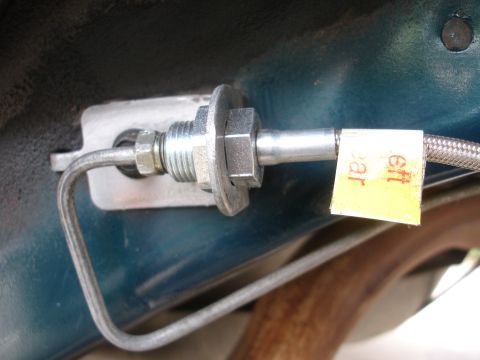 1995 Ford Taurus - A close-up view of a metal brake line fitting attached to a vehicle's chassis, with a yellow tag indicating 'left rear'.