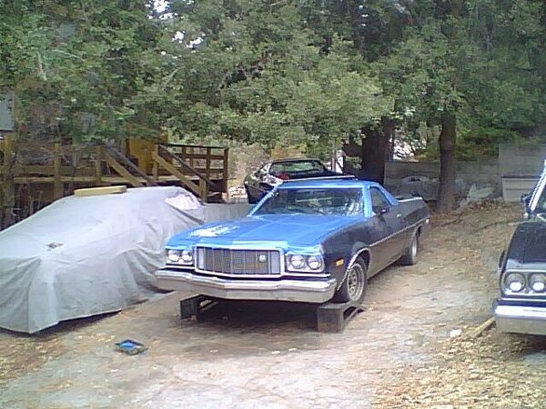 Blue pickup truck on blocks, another car covered, and a black car partially visible