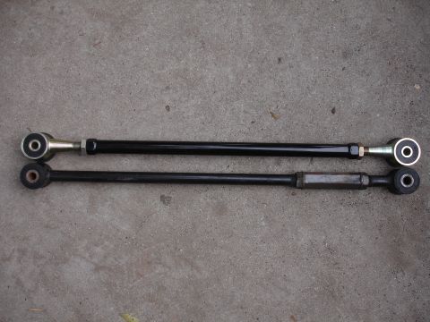 1995 Ford Taurus - Two aftermarket suspension control arms are laid out side-by-side on a gray concrete surface.
