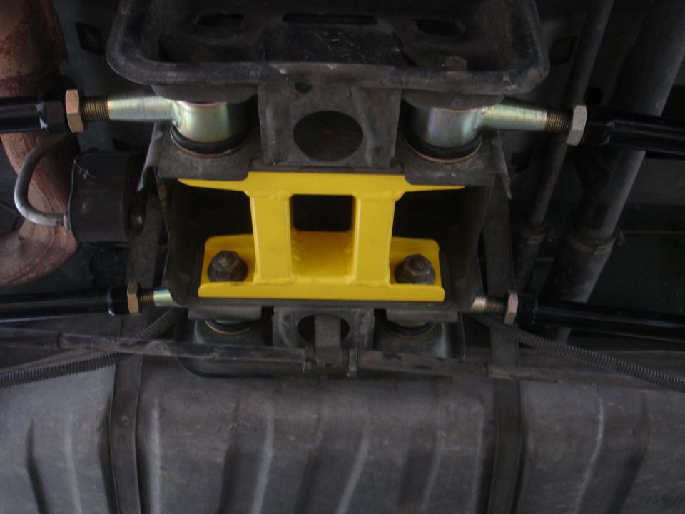 underbody shot of yellow rear suspension brace with black tie rods and fuel tank visible