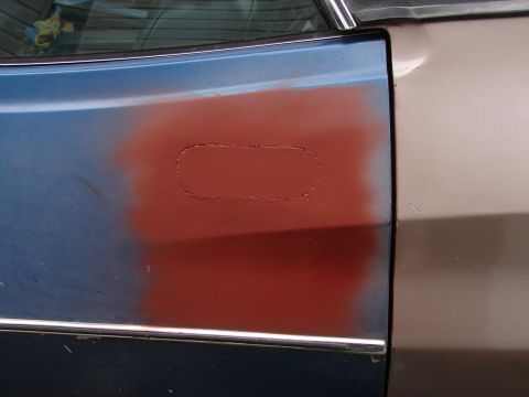 1973 Ford Ranchero - Close-up of a car door showing a patch of red primer over blue paint, with a chrome trim piece.