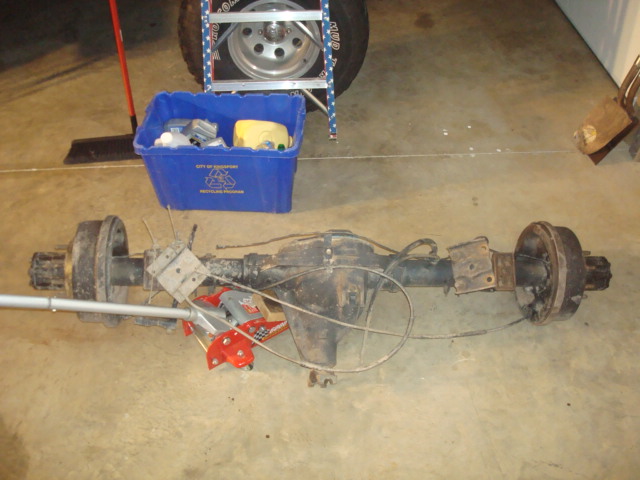 Rear axle assembly with drum brakes and brake lines, on a concrete floor
