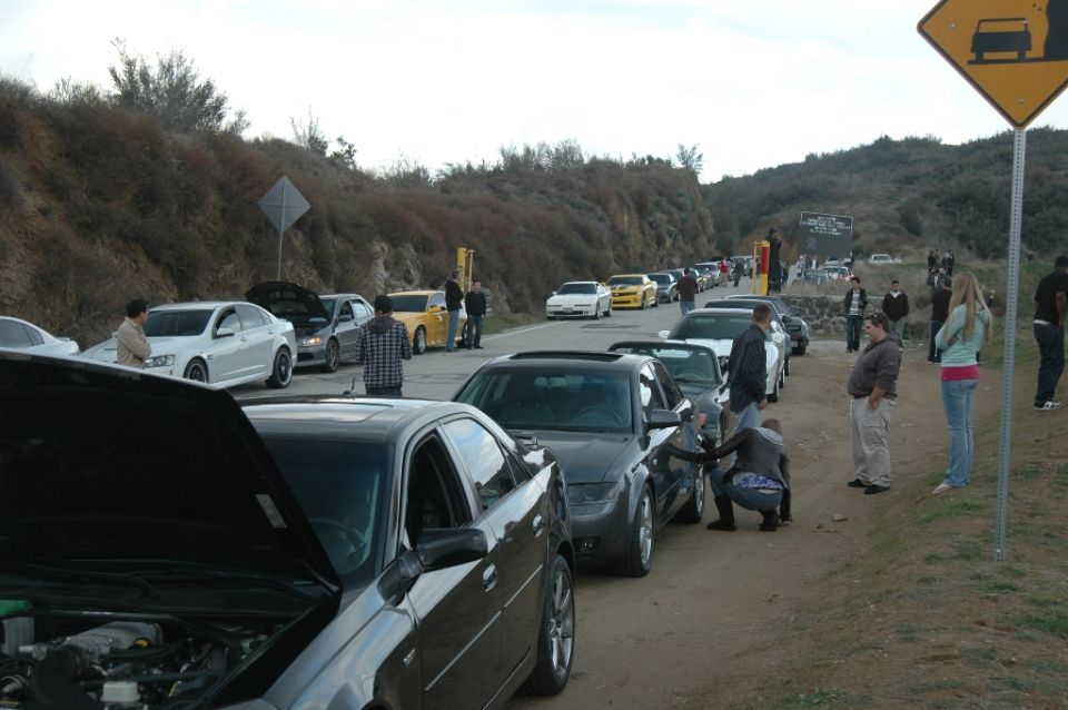 Roadside canyon car meet with hoods open, black and silver sedans and spectators