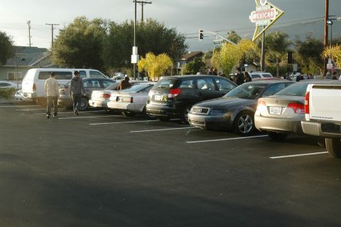 2006 Cadillac STS - A variety of vehicles are parked in a lot under a bright sky, with a neon sign visible in the distance.