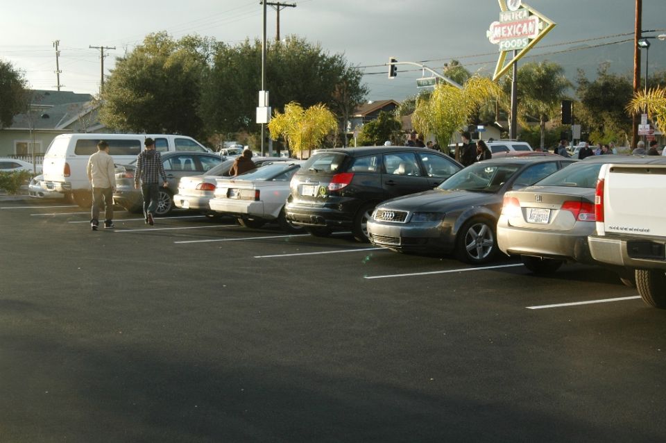 Cars parked in a lot at dusk beside a neon Tolteca Mexican Foods sign
