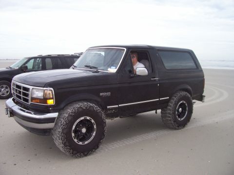 1994 Ford Bronco - 1994 Ford Bronco parked on the sand with a second vehicle in the background.