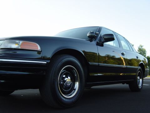 1996 Ford Crown Victoria - A black 1996 Ford Crown Victoria is shown from a low angle, highlighting its front fender and wheel.