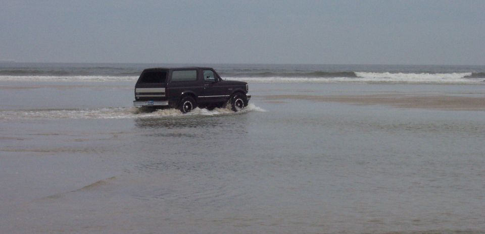 Dark 1994 Ford Bronco driving on a beach