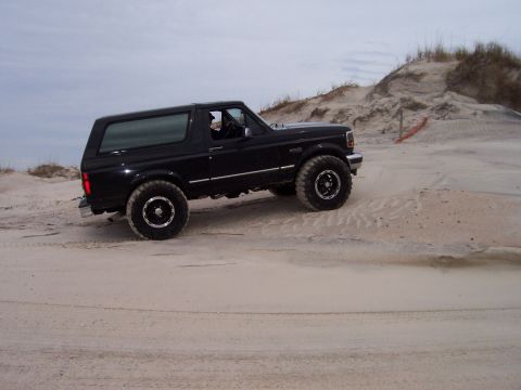 1994 Ford Bronco - 1994 Ford Bronco navigating sand dunes under an overcast sky.