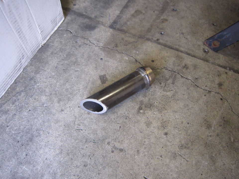 Metal exhaust tip with angled opening, lying on a concrete floor