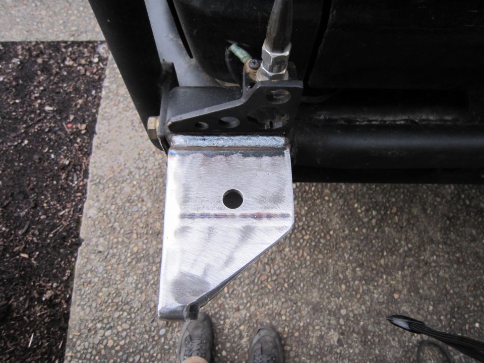 Close-up of a custom-welded metal bracket attached to a black frame tube, with a single bolt hole