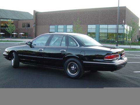 1996 Ford Crown Victoria - A black sedan is parked in a lot with a brick building in the background.