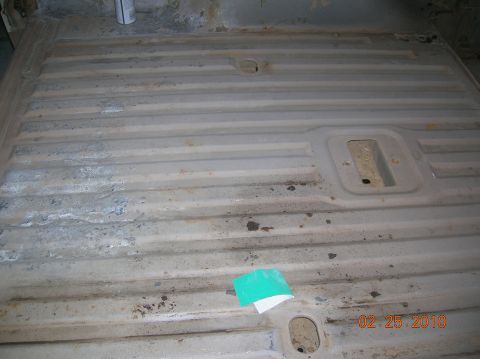 1985 Ford Bronco - The interior floor pan of a vehicle shows signs of wear and tear, with a sanding pad resting on it.