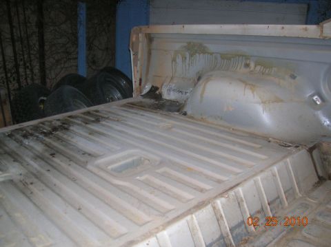 1985 Ford Bronco - The interior of a truck bed shows signs of wear and tear, with tires stacked nearby.