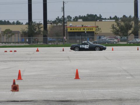 2003 Mazda Protege - A dark-colored convertible with racing numbers is on a course marked by orange cones, with a Waffle House in the background.