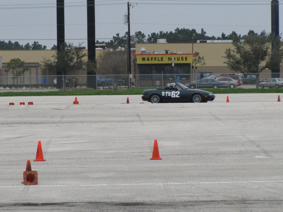 Black convertible sports car with STS 62 on the side, on a paved lot with cones