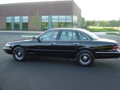 1996 Ford Crown Victoria - A black 1996 Ford Crown Victoria sedan is parked in front of a modern brick building.