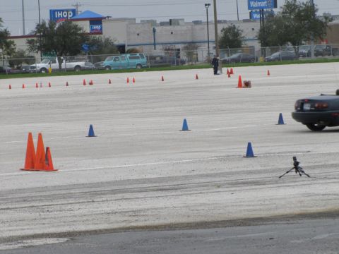 2003 Mazda Protege - A dark convertible sports car navigates a course marked by traffic cones in a parking lot.