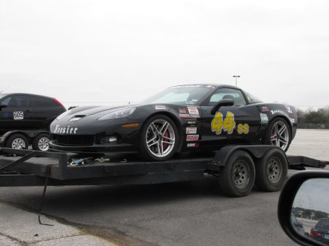 2003 Mazda Protege - A black Chevrolet Corvette, adorned with racing decals and the number 44 SS, is transported on a trailer.