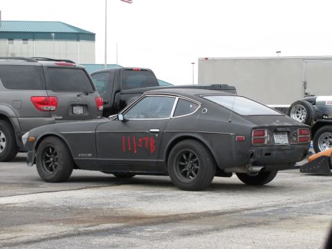 2003 Mazda Protege - A Datsun 280Z is parked next to other vehicles, showing custom red markings on its door.