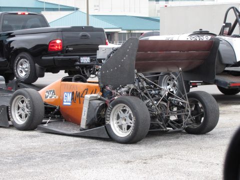 2003 Mazda Protege - A custom-built open-wheel race car is parked next to a black pickup truck.