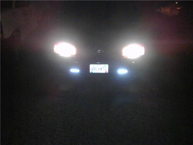 Front of a sedan at night with bright headlights, blue fog lights, and a center license plate