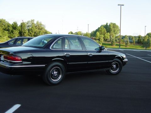 1996 Ford Crown Victoria - A black 1996 Ford Crown Victoria is parked in an empty lot with trees in the background.