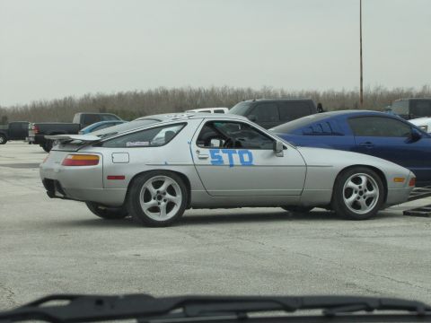 2003 Mazda Protege - Silver Porsche 928 with blue 'STO' text on its side, parked outdoors with other vehicles.