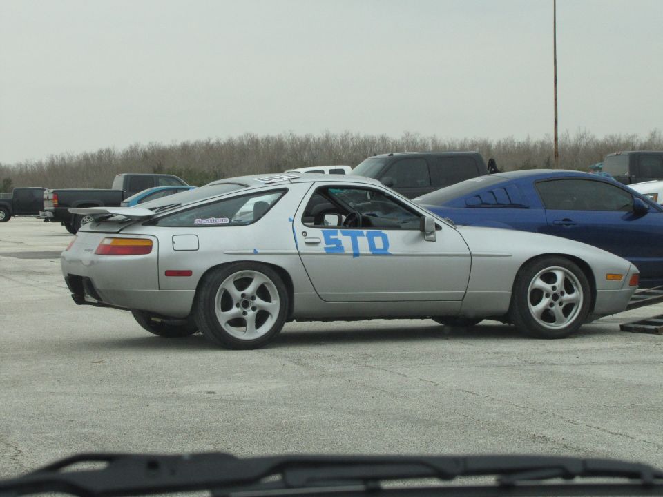 Silver Porsche 928 with blue 'STO' text on the side, parked next to a blue car