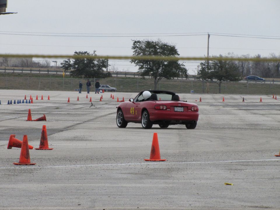 Red convertible sports car with number 49 on the door, driving on a track with orange cones