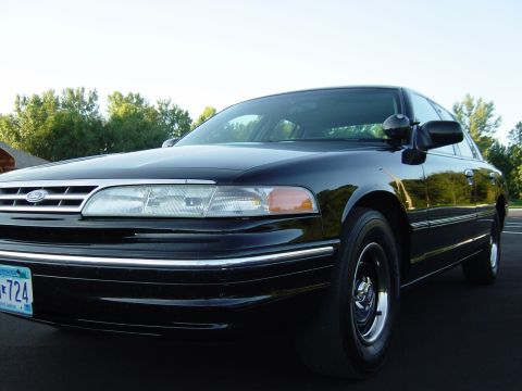 1996 Ford Crown Victoria - A black Ford Crown Victoria is shown from the front quarter angle with a clear sky and trees in the background.