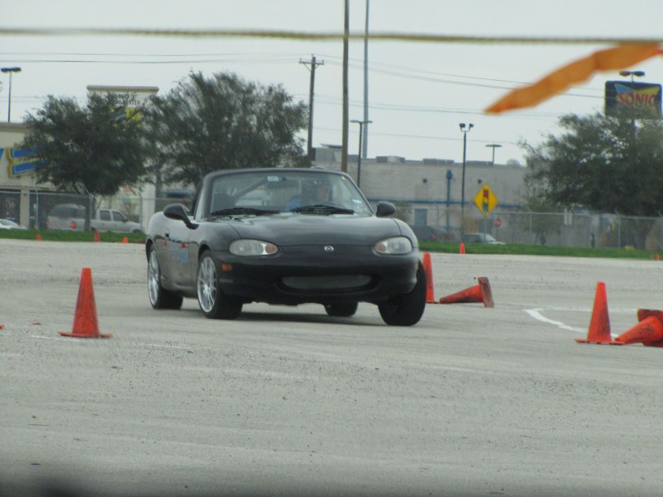 Black convertible sports car with a soft top, viewed from the front at an autocross event