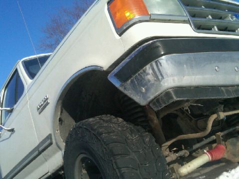 1987 Ford Bronco - Front quarter view of a white Ford truck, showing the fender, tire, and front bumper.