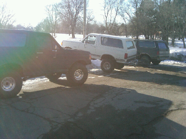 Black SUV in foreground, white SUV and dark SUV behind it, parked on asphalt with snow on the ground