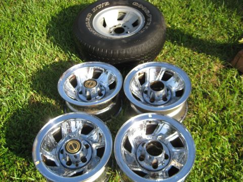 1995 Ford Bronco - Set of four chrome wheels and a spare tire, likely for sale, displayed on a grassy surface.
