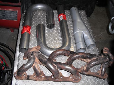 1991 Ford Bronco - Several exhaust system components, including manifolds and various pipe sections, are arranged on a metal surface.