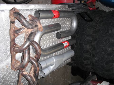 1991 Ford Bronco - A collection of exhaust system parts, including a manifold and various pipes, are laid out on a textured surface.