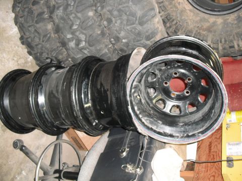 1991 Ford Bronco - Several large tires and multiple black rims are piled together indoors.