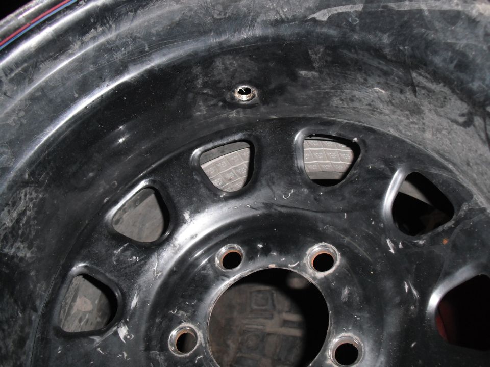 Black steel wheel rim with lug nut holes and a valve stem hole