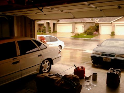 1989 Ford Taurus - Three cars are parked inside a garage on a rainy day, with houses visible outside.