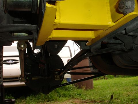 1995 Ford Taurus - The photo shows the rear suspension of a vehicle, with a yellow brace installed. A Ford emblem is visible on another vehicle in the backgro…