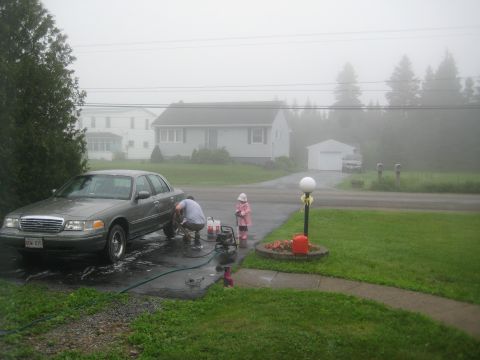 1999 Ford Crown Victoria - A father washes his 1999 Ford Crown Victoria in the driveway while his child watches, on a foggy day.